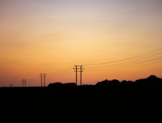 Power distribution lines and utility poles silhouetted at dusk, the kind of circuits SCE de-energizes during a public safety power shutoff