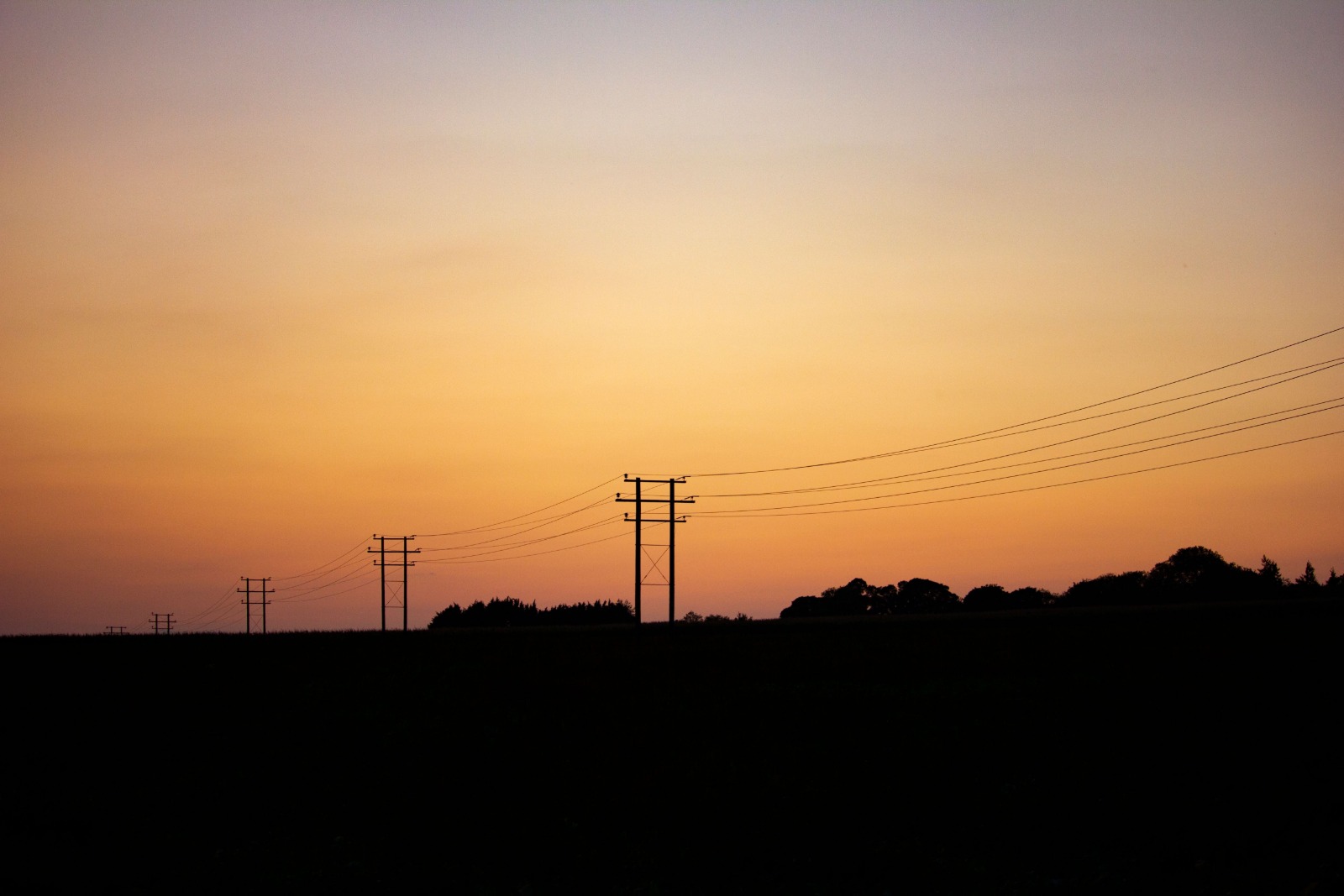 Power distribution lines and utility poles silhouetted at dusk, the kind of circuits SCE de-energizes during a public safety power shutoff
