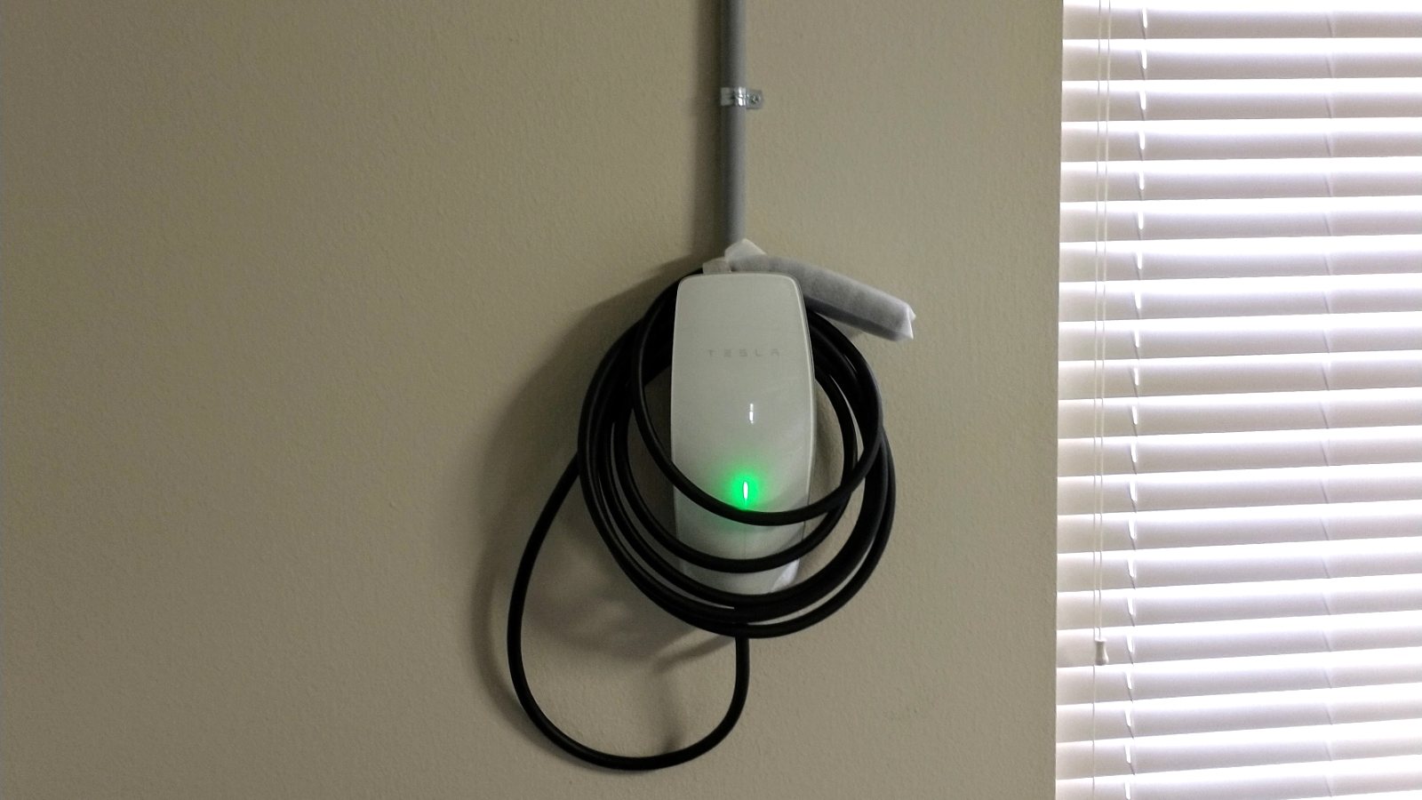 Tesla Wall Connector mounted on a garage wall with conduit and coiled charging cable