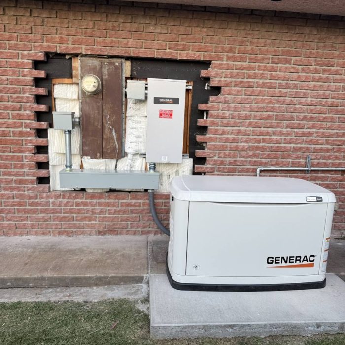 Generac home standby generator on a concrete pad beside a brick wall, with its automatic transfer switch mounted next to the electric meter
